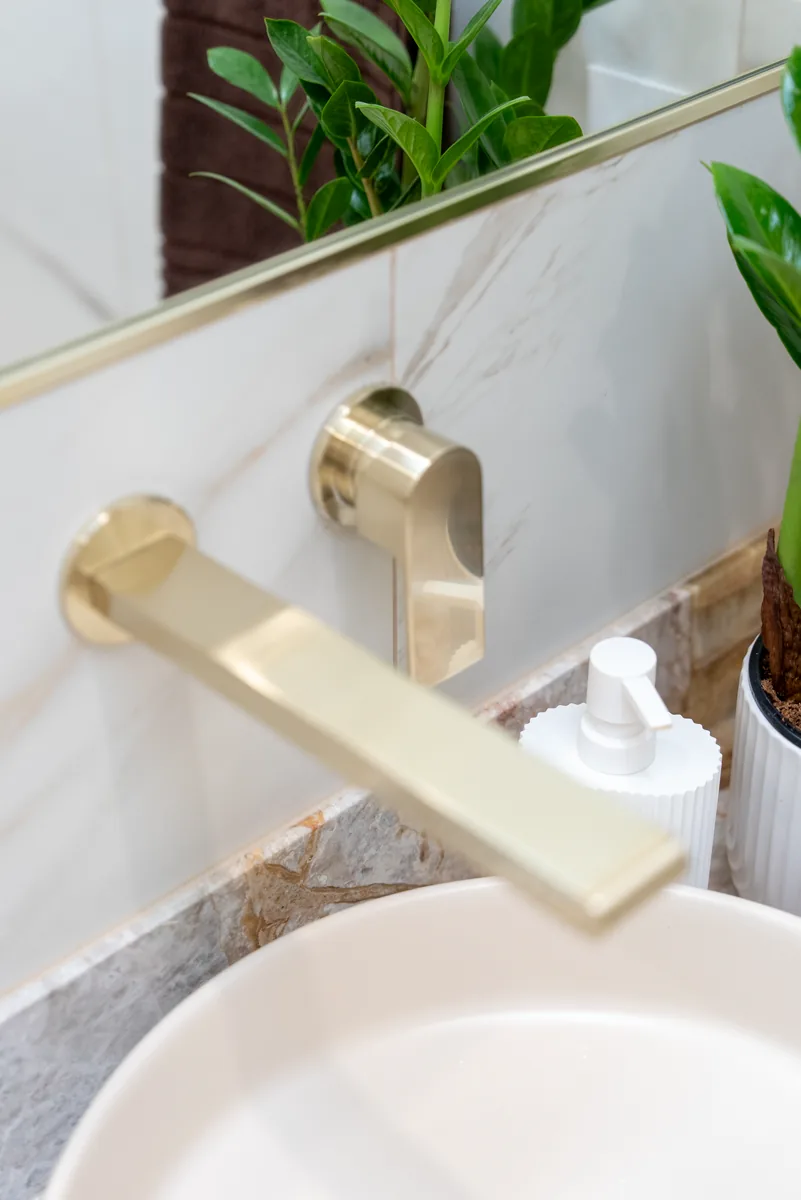 Brushed brass wall mixer against marble tiling